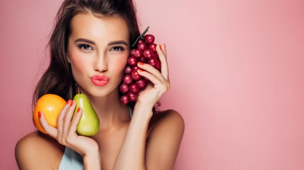 A pregnant woman showcasing her most common food cravings with a vivid display of fruit on a vibrant pink background.