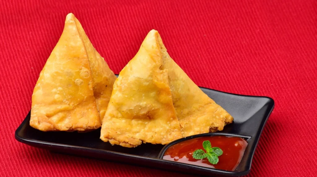 Most common food cravings during pregnancy: Two samosas on a black plate with sauce.
